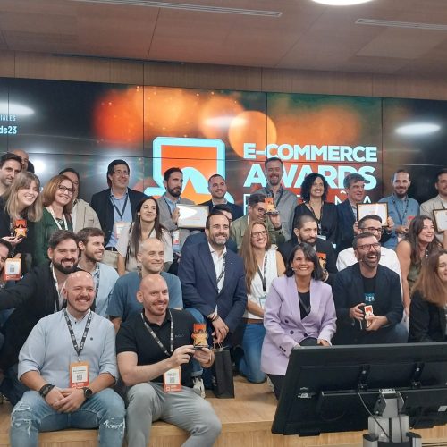 Grupo de personas sonrientes posan con trofeos y certificados en un evento de premios de comercio electrónico. Texto: "E-COMMERCE AWARDS ESPAÑA 2023", "#EcommerceAwards23".