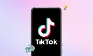 Sobre un fondo degradado azul y rosa, aparece un teléfono móvil en cuya pantalla se ve el logo de TikTok. Junto al teléfono hay un emoji de un robot y otro de una bombilla encendida