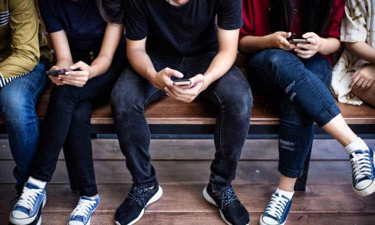 Personas sentadas usando smartphones, concentradas en sus dispositivos, en un banco de madera. Perfecto para ilustrar temas de conexión digital y tecnología.