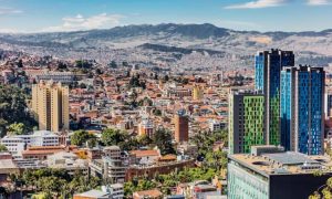 Edificios altos destacan en una densa ciudad, rodeada de montañas bajo un cielo despejado. Ideal para campañas de turismo urbano y exploración.