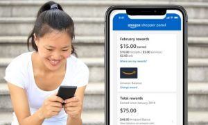 Mujer sonríe mirando un móvil; pantalla muestra recompensas de Amazon Shopper Panel. Fondo: escaleras. Texto: "$15.00", "Total rewards", "February rewards". Marketing digital.