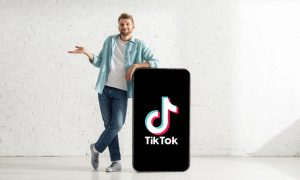 Fotografía de un hombre blanco y rubio de unos 30 años que está apoyado en un teléfono gigante en cuya pantalla aparece el logo de TikTok