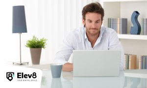 Fotografía de un hombre sentado en su luminoso despacho y utilizando su ordenador para cursar el programa de eCommerce Specialist de Elev8