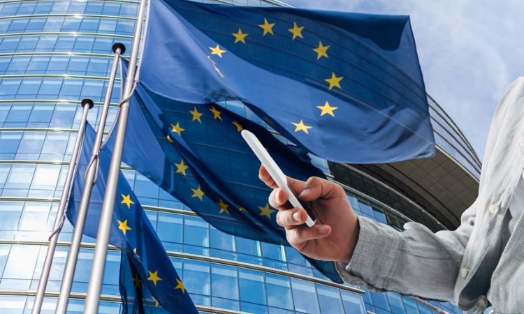 una mano usando el móvil ante una bandera de la ue, q lanza su nueva dma