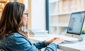 Persona trabajando en ordenador, enfocada en pantalla en oficina moderna; concepto de productividad y conexión digital.