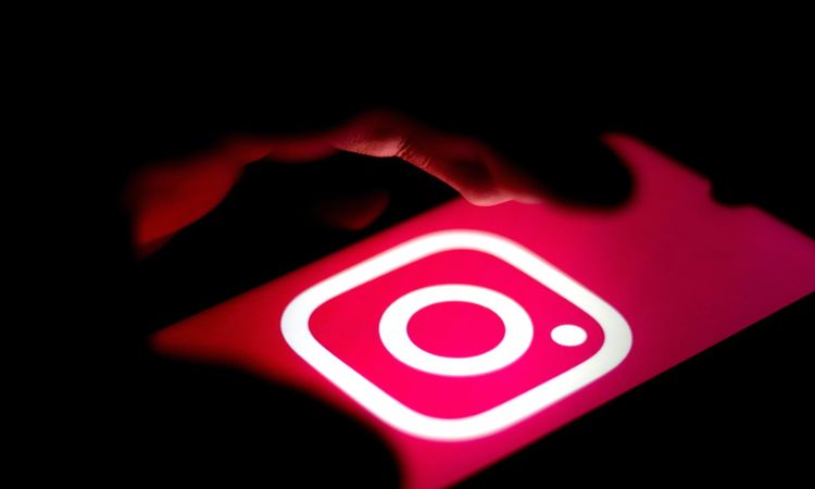 Fotografía de una mano sobre un teléfono móvil en cuya pantalla aparece el logo de Instagram. La atmósfera es oscura y la única luz proviene de la pantalla del móvil, representando que la persona está a punto de eliminar su cuenta de Instagram
