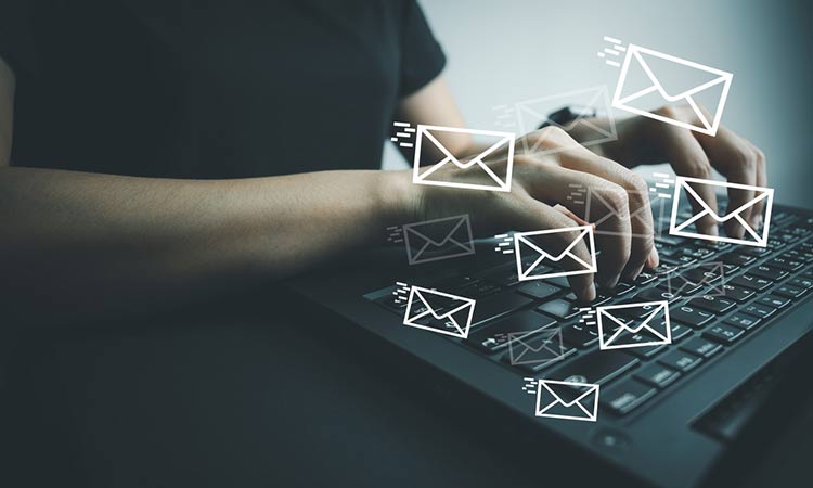 Manos tecleando en un portátil, rodeadas de iconos de mensajes flotantes. Contexto de comunicación digital y marketing por correo electrónico.