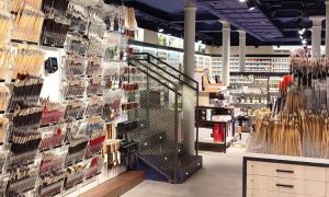 Tienda de arte con pinceles organizados en estantes, escaleras al fondo, rodeada de materiales artísticos, ambiente ordenado e inspirador para pintar.