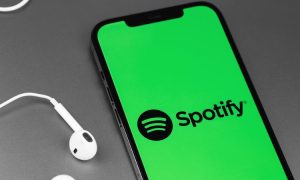 Fotografía en la que, junto a unos auriculares, aparece un teléfono móvil en cuya pantalla se está iniciando la app de Spotify, de la que vamos a contar su historia