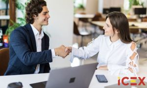 Personas dándose la mano, simbolizando acuerdo, en oficina moderna con portátil y móvil en mesa. Logotipo ICEX visible. Keywords: negocio, colaboración.