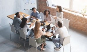 Fotografía en plano aéreo picado de un equipo de publicidad conformado por hombres y mujeres de diversas etnias. Estos profesionales están sentados alrededor de una mesa repleta de documentos y material de oficina, y junto a una pizarra, analizando el estado de la inversión publicitaria en España en enero de 2025