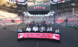 Captura del directo de la Velada del Año 5. En un plano aéreo se muestra el escenario en el que estaban Ibai y los otros comentaristas del evento. En la mesa en la que están se ven los logos de las marcas patrocinadoras.