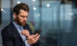 Fotografía de un hombre de unos 40 años que mira su teléfono móvil sorprendido e indignado