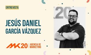 La imagen muestra un diseño dividido en dos partes: a la izquierda, el texto “ENTREVISTA” en una etiqueta destacada, seguido por el nombre “JESÚS DANIEL GARCÍA VÁZQUEZ” en letras grandes azules. Debajo aparece el logotipo de MK20 | Agencia de Marketing en naranja. A la derecha, hay una foto en blanco y negro de Jesús Daniel, con gafas, barba y brazos cruzados.
