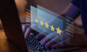 Manos tecleando en portátil; sobre teclado flotan 5 estrellas amarillas; entorno oscuro. Contexto de reseñas online y satisfacción del cliente.