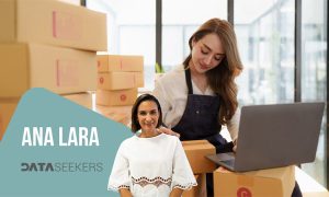 Mujer usando portátil rodeada de cajas. En primer plano, retrato de otra mujer. Texto: "ANA LARA DATASEEKERS". Contexto de entorno laboral logístico.