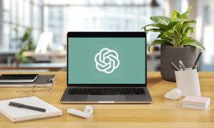 En la pantalla de un ordenador portátil se ve el símbolo de ChatGPT. El ordenador está colocado sobre una mesa en el interior de una oficina luminosa.