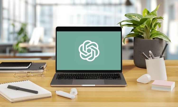 En la pantalla de un ordenador portátil se ve el símbolo de ChatGPT. El ordenador está colocado sobre una mesa en el interior de una oficina luminosa.