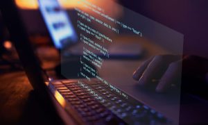 Portátil mostrando código en pantalla, mano tecleando, ambiente oscuro. Texto de programación, desarrollo software, tecnología digital.