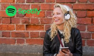 Una mujer aparece sentada y escuchando música con unos cascos junto a un muro de ladrillo a la derecha de la imagen. En la parte superior izquierda aparece el logo de Spotify