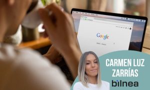 En la imagen se ve a una persona de espaldas, tomando café mientras trabaja con un portátil abierto en el que aparece la página principal de Google. En primer plano, en la parte inferior derecha, hay un diseño gráfico circular en color verde azulado que incluye la foto de una mujer rubia de cabello liso, junto a su nombre en letras blancas: Carmen Luz Zarrías, acompañado del logotipo de bilnea. La composición combina una escena cotidiana de trabajo digital con un refuerzo visual que destaca a la profesional y a la agencia, transmitiendo la idea de especialización en SEO y marketing digital.