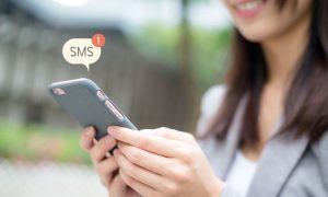 Imagen de una mujer española joven sosteniendo un smartphone mientras del mismo sale una notificación que nos indica que ha recibido un SMS.