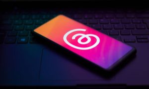 Fotografía de un teléfono móvil apoyado sobre un teclado de ordenador portátil. La escena es oscura y la única luz proviene de la pantalla del teléfono, en la que se muestra el icono de Threads, red social de Meta que ha alcanzado los 300 millones de usuarios activos mensuales